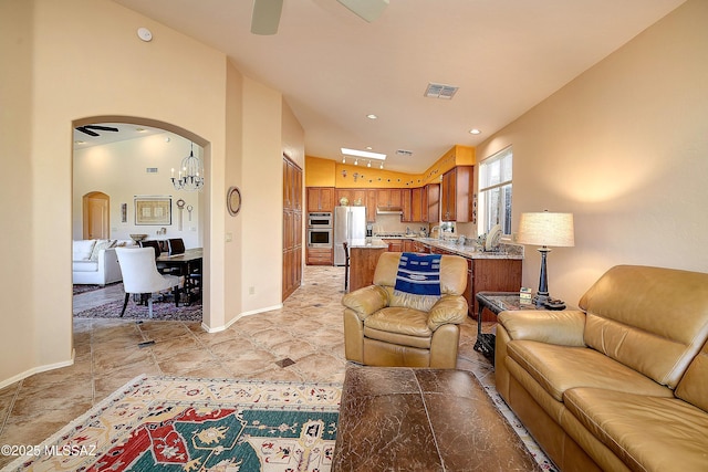 living area with arched walkways, ceiling fan with notable chandelier, visible vents, baseboards, and vaulted ceiling