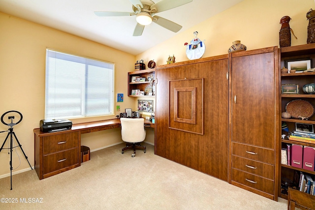 carpeted office with lofted ceiling, built in desk, and a ceiling fan