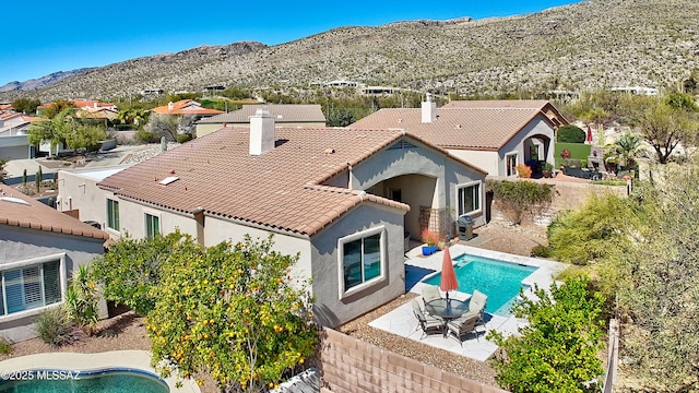 back of house with a tile roof, a chimney, stucco siding, a patio area, and a mountain view