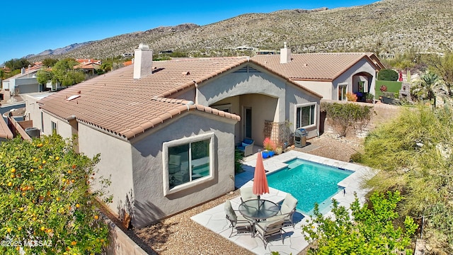 back of property featuring a mountain view, a tile roof, stucco siding, a chimney, and a patio area