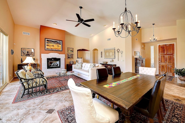 dining area with arched walkways, high vaulted ceiling, ceiling fan with notable chandelier, and a tiled fireplace