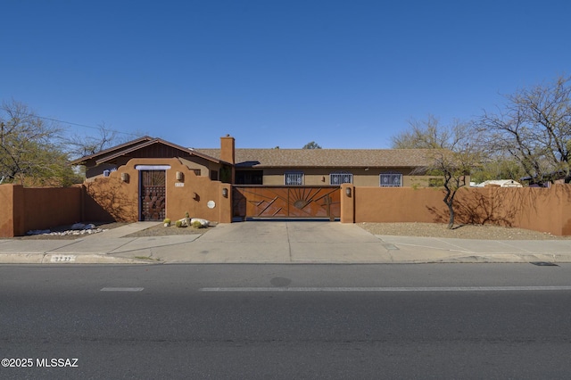 view of front facade with a gate, driveway, stucco siding, a chimney, and a fenced front yard