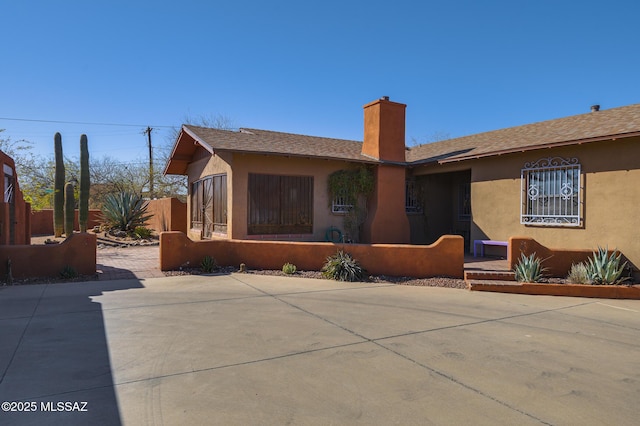 view of front of property with stucco siding, a chimney, a patio, and fence