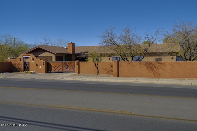 view of front facade featuring a fenced front yard, concrete driveway, a chimney, and a gate