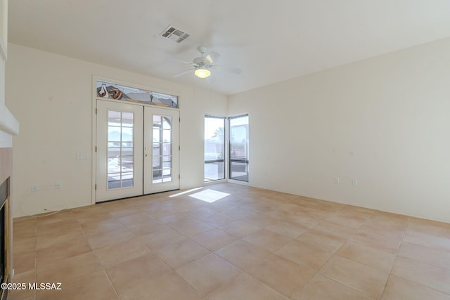 spare room featuring light tile patterned floors, a fireplace, visible vents, a ceiling fan, and french doors