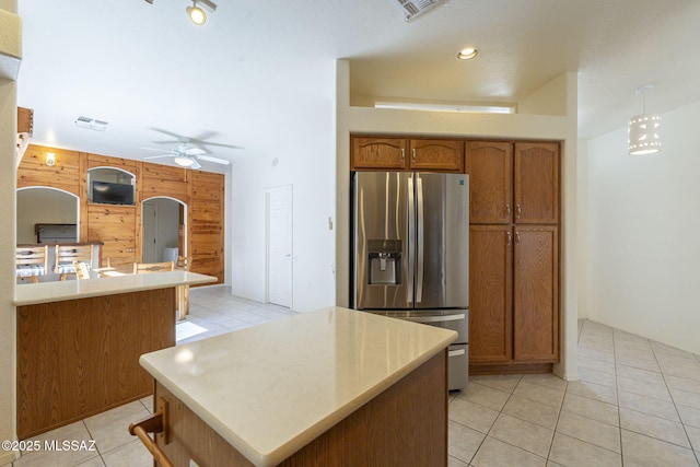 kitchen featuring light tile patterned floors, a ceiling fan, stainless steel fridge with ice dispenser, brown cabinets, and light countertops