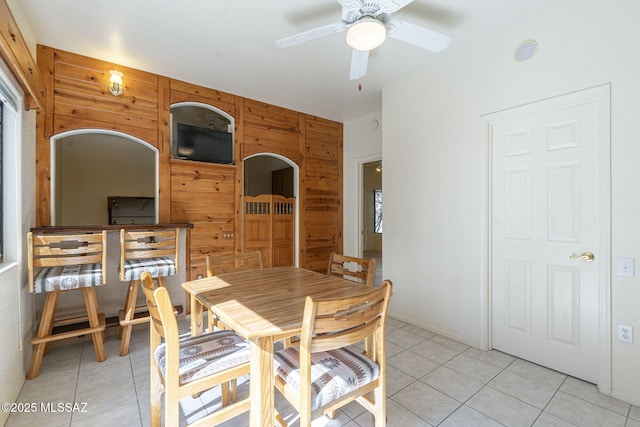 dining space with light tile patterned floors, ceiling fan, and wood walls