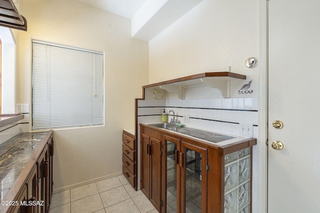 kitchen with baseboards, glass insert cabinets, a sink, and light tile patterned flooring