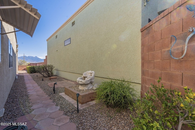 view of side of home featuring fence, a mountain view, and stucco siding