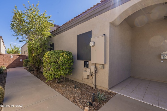 view of side of property with a patio area, a tiled roof, fence, and stucco siding