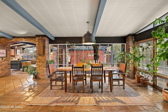 dining space featuring brick wall and beamed ceiling