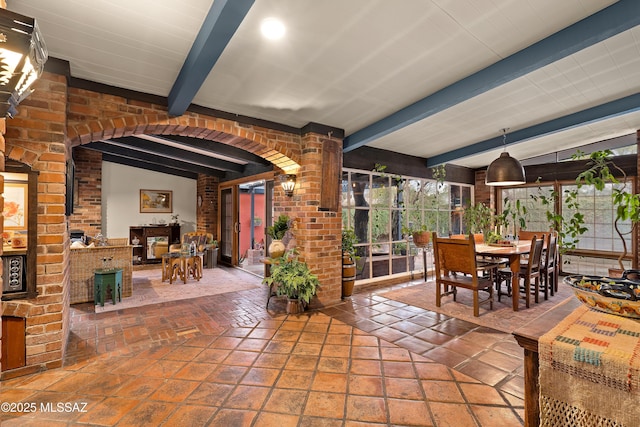 dining space with lofted ceiling with beams, brick wall, arched walkways, and a wealth of natural light