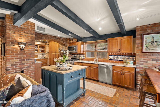 kitchen featuring brick wall, butcher block countertops, appliances with stainless steel finishes, brick floor, and a sink