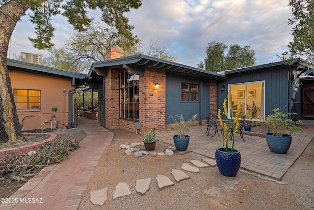 back of property with a patio, brick siding, and a chimney