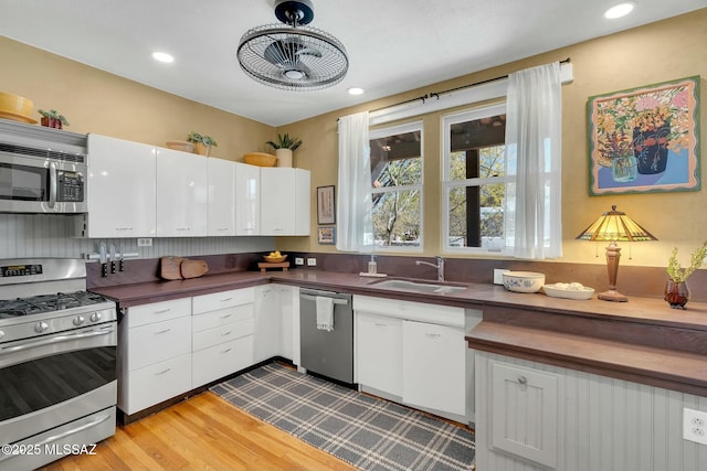 kitchen with stainless steel appliances, dark countertops, a sink, and white cabinetry