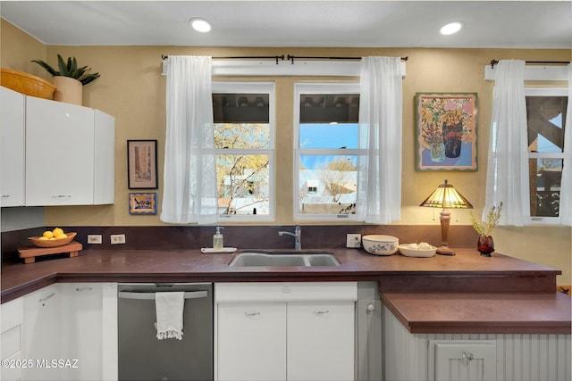 kitchen with dark countertops, recessed lighting, white cabinetry, a sink, and dishwasher