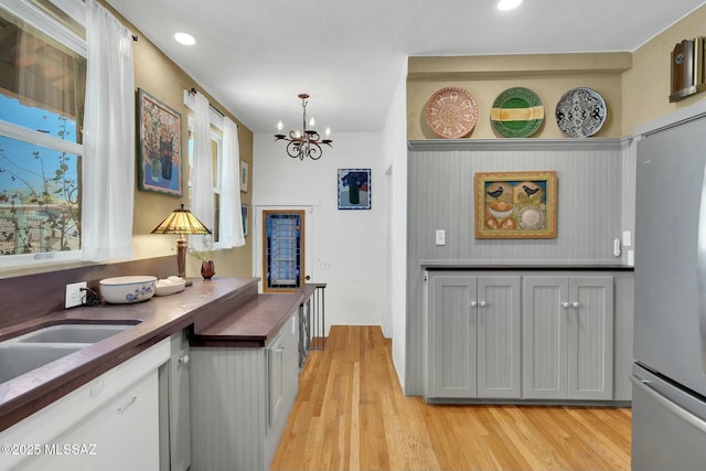 kitchen with dark countertops, freestanding refrigerator, an inviting chandelier, light wood-type flooring, and recessed lighting