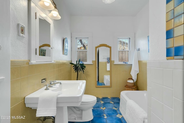 full bathroom with toilet, a wainscoted wall, tile walls, and a bath