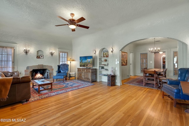 living area featuring a warm lit fireplace, a textured ceiling, built in shelves, arched walkways, and wood finished floors