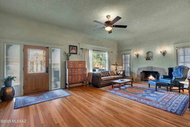 living area with a lit fireplace, a textured ceiling, wood finished floors, and a textured wall