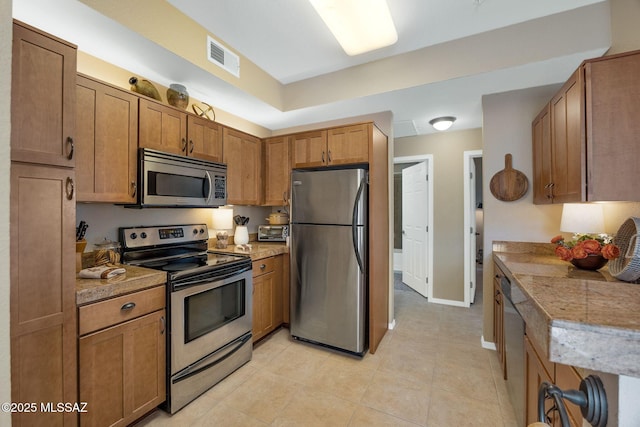 kitchen featuring brown cabinets, light tile patterned floors, stainless steel appliances, visible vents, and baseboards