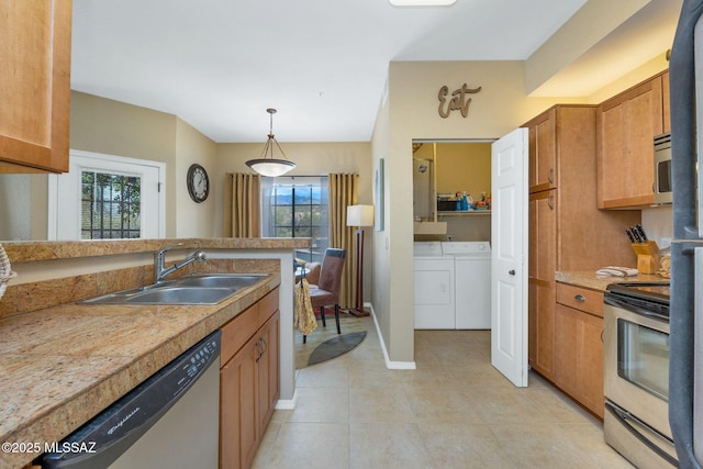 kitchen featuring decorative light fixtures, light countertops, appliances with stainless steel finishes, washing machine and dryer, and a sink