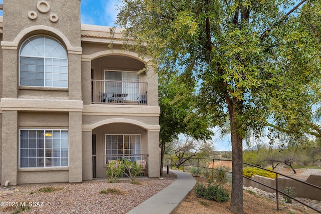 view of front of house with fence, a balcony, and stucco siding