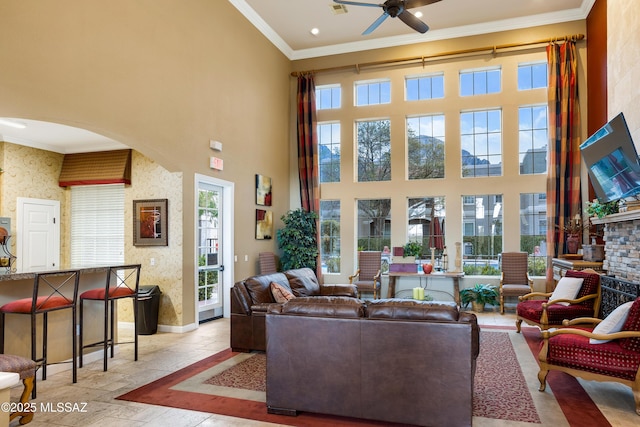 living room featuring arched walkways, a high ceiling, baseboards, stone tile flooring, and crown molding