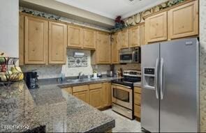 kitchen featuring a peninsula, stainless steel appliances, light brown cabinetry, stone counters, and a sink