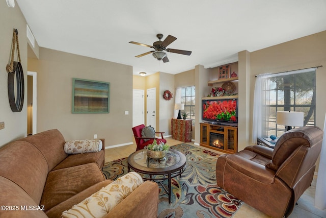 tiled living area featuring baseboards, a ceiling fan, and a glass covered fireplace