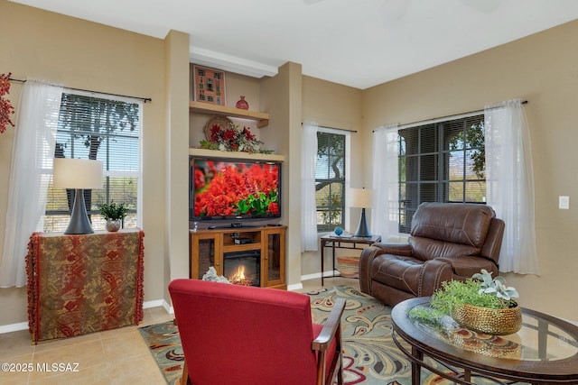 living area with baseboards, a glass covered fireplace, and tile patterned floors