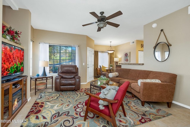 living room featuring light tile patterned floors, visible vents, a glass covered fireplace, ceiling fan, and baseboards