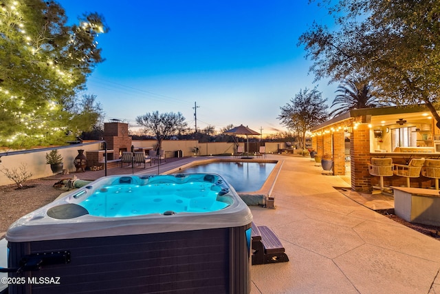 pool at dusk with fence, outdoor dry bar, a fenced in pool, a patio area, and a hot tub