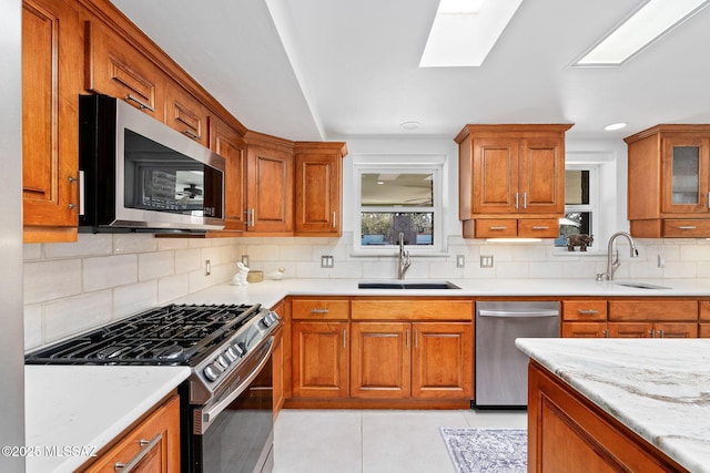 kitchen with appliances with stainless steel finishes, brown cabinetry, a sink, and backsplash