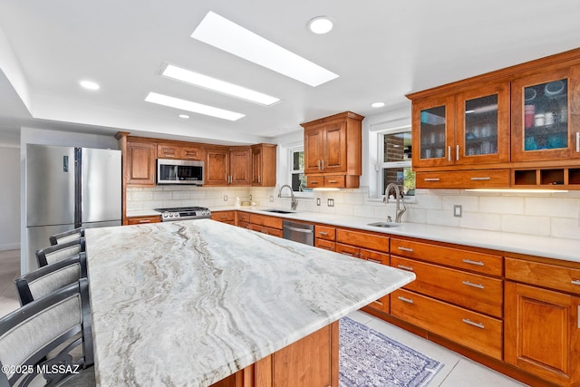 kitchen with tasteful backsplash, appliances with stainless steel finishes, brown cabinetry, and a sink