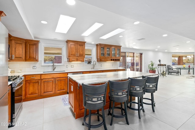 kitchen featuring stainless steel range with gas cooktop, brown cabinets, a sink, and a breakfast bar area