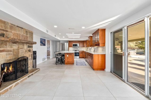 kitchen featuring a breakfast bar area, appliances with stainless steel finishes, brown cabinets, light countertops, and a stone fireplace