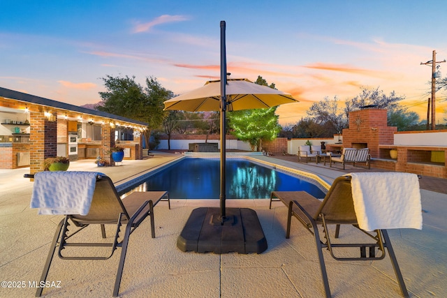 view of pool with a brick fireplace, a patio area, fence, and a fenced in pool