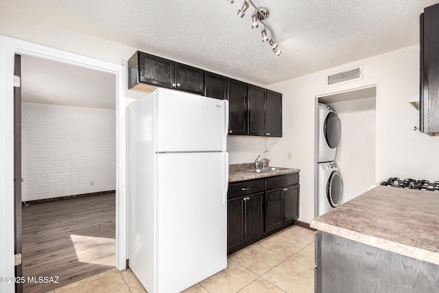 kitchen with stacked washer and clothes dryer, visible vents, a sink, freestanding refrigerator, and brick wall