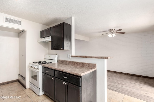 kitchen with under cabinet range hood, visible vents, baseboards, brick wall, and white range with gas stovetop