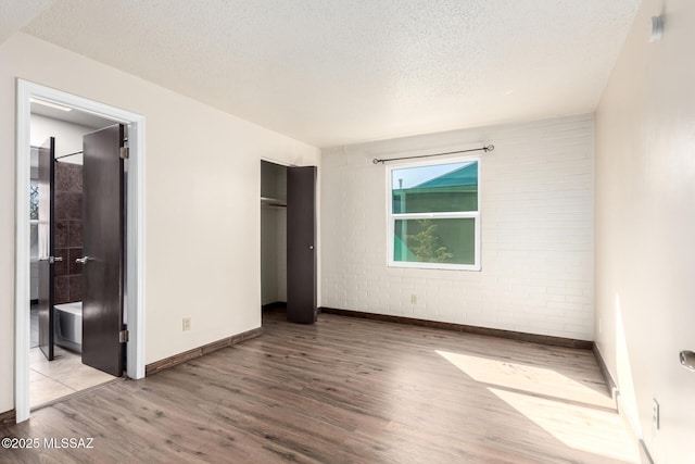 unfurnished bedroom with wood finished floors, baseboards, a textured ceiling, brick wall, and ensuite bathroom