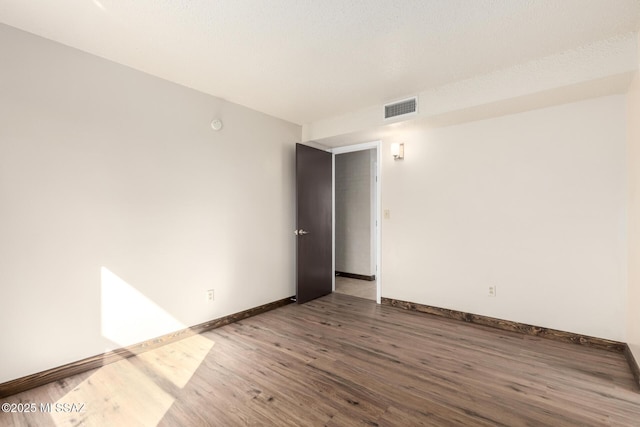 spare room featuring baseboards, wood finished floors, and visible vents