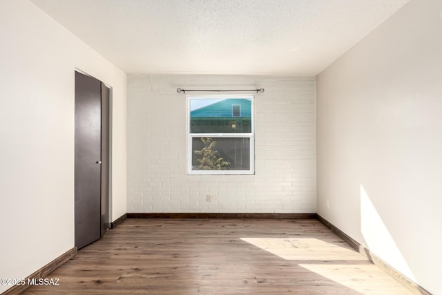 spare room featuring baseboards, wood finished floors, brick wall, and a textured ceiling