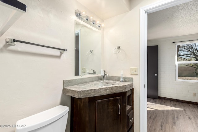 half bathroom with toilet, vanity, wood finished floors, and a textured ceiling
