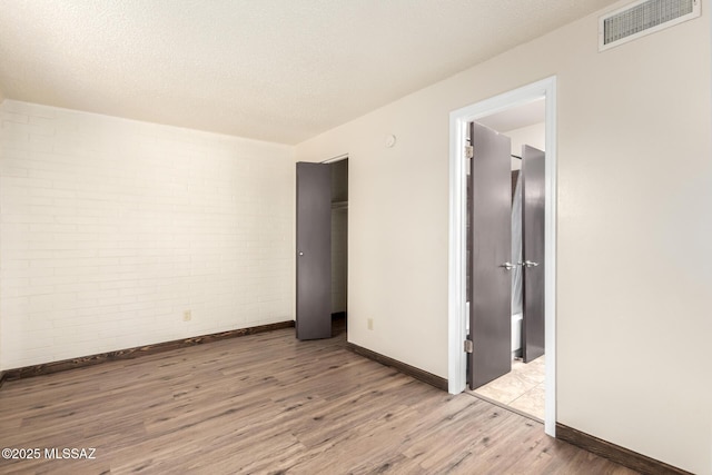 unfurnished bedroom with brick wall, baseboards, wood finished floors, and visible vents