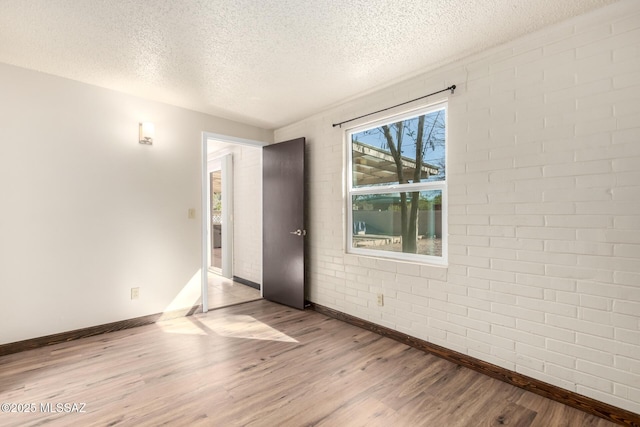empty room with baseboards, wood finished floors, a textured ceiling, and brick wall