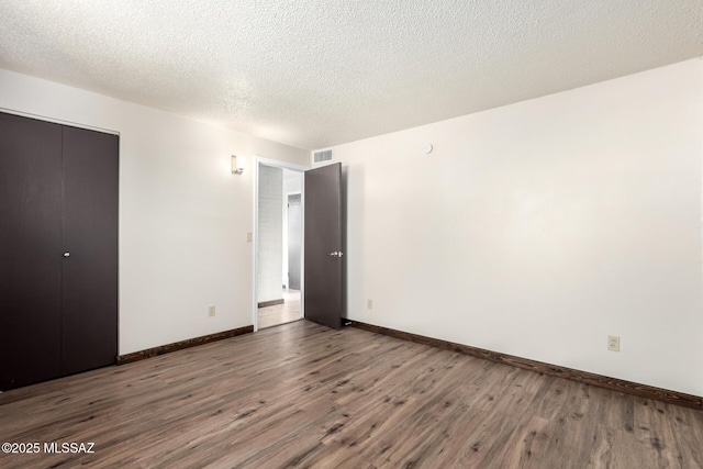 unfurnished bedroom with baseboards, wood finished floors, visible vents, and a closet