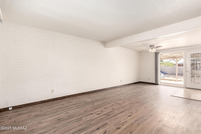 empty room featuring wood finished floors, a ceiling fan, baseboards, a textured ceiling, and brick wall