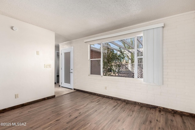 spare room with wood finished floors, a textured ceiling, baseboards, and brick wall