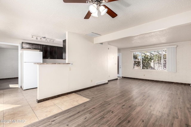 unfurnished living room featuring brick wall, a ceiling fan, a textured ceiling, and light wood-type flooring
